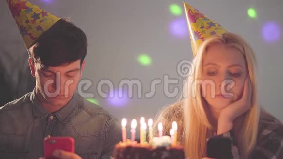 肖像悲伤的女孩和一个戴着生日帽的男人坐在蛋糕前手里拿着蜡烛发短信视频的预览图