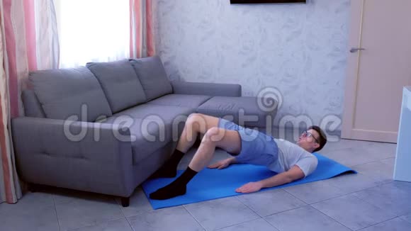 有趣的书呆子男子正在做臀部桥梁运动的垫子以加强肌肉的腿在家里体育幽默视频的预览图