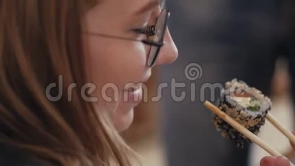 靠近一个戴眼镜的年轻女人的脸她用筷子吃日本卷视频的预览图