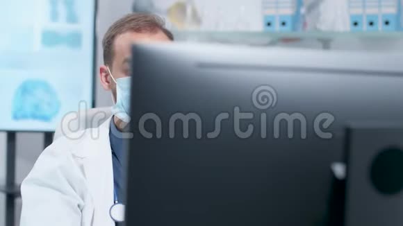 手持照片的医生戴着药用面具在电脑上工作视频的预览图