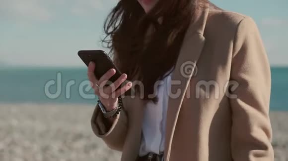 快乐的黑发女人正在海滩上展示智能手机特写镜头视频的预览图