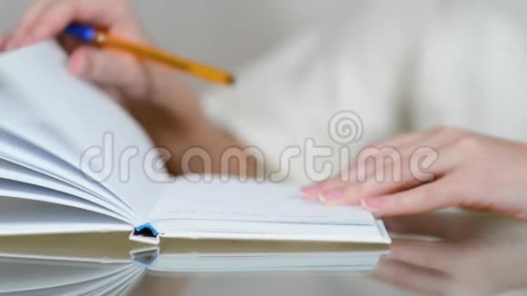 一个女人在笔记本上做笔记然后关闭它并从桌子上移除它视频的预览图