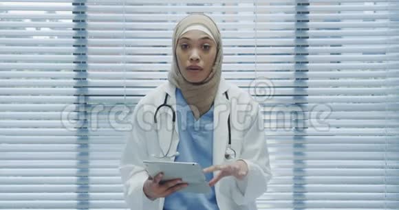 年轻的女医生用平板电脑和摄像机交谈视频的预览图
