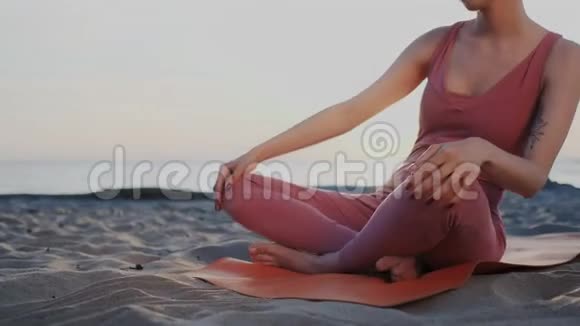 年轻女子在海滩上打坐莲花姿势热身身体揉捏脊椎肌肉运动女孩视频的预览图