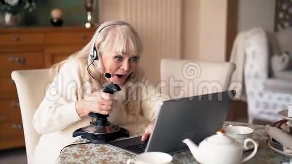 戴耳机的奶奶在室内玩电脑游戏视频的预览图