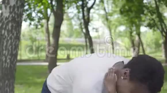 肖像非裔美国妇女把她的儿子搂在怀里在绿色公园里紧紧地抱着两人都笑了可爱的儿童视频的预览图