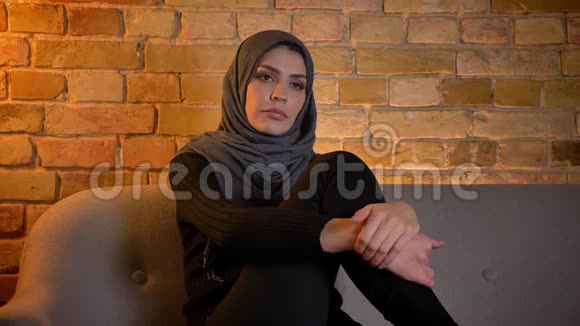 戴着头巾看电视坐在室内沙发上悲伤的成年穆斯林女性特写照片视频的预览图