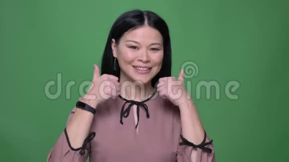 年轻迷人的亚洲女性特写镜头黑发微笑着用拇指指着背景说是视频的预览图