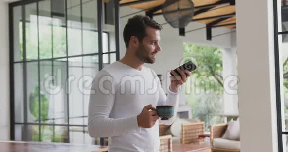 男人拿着咖啡杯在舒适的家里用手机说话视频的预览图