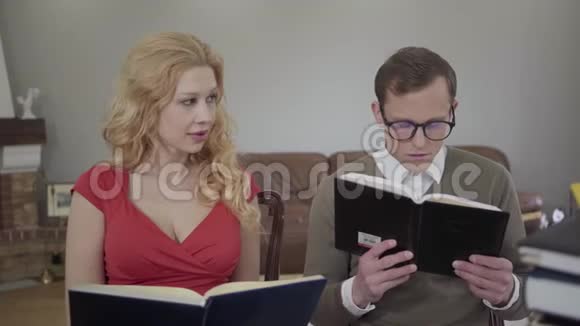 年轻端庄的男人戴着眼镜卷曲的金发女人坐在沙发上看书书呆子倒下了视频的预览图