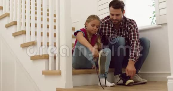 父亲在一个舒适的家里帮助女儿在楼梯上穿鞋视频的预览图