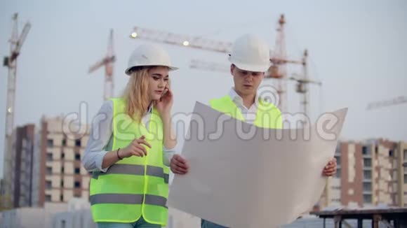 女人在打电话问建筑工人在下面的建筑物背景上的图纸上有什么视频的预览图