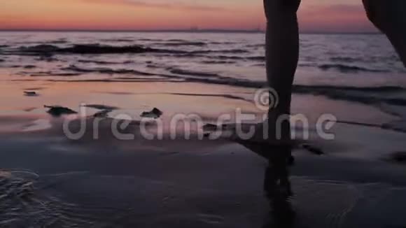夕阳西下光着脚在沙滩上散步的美丽女子特写镜头热带海岸度假红色的天空水视频的预览图