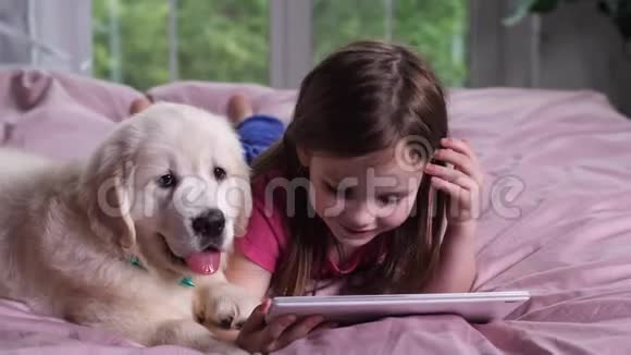 微笑的女孩和小狗一起看平板电脑上的卡通视频的预览图