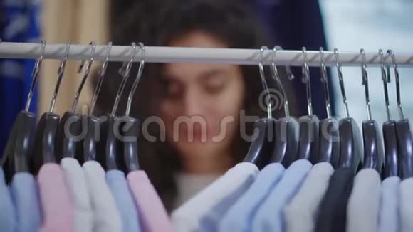 挂着t恤的衣架在架子上女人在挑选衣服不集中的脸视频的预览图