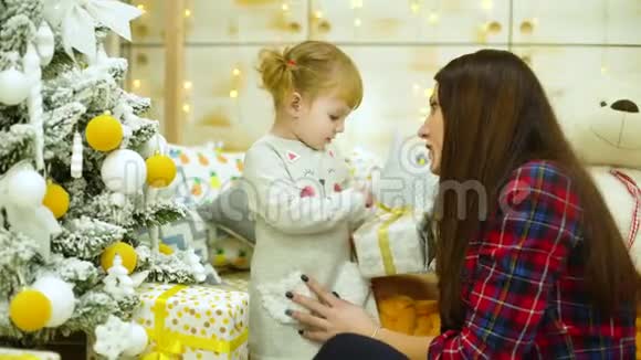 小女孩带着妈妈在家附近的圣诞树上打开礼物盒视频的预览图
