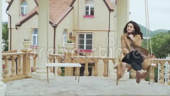 穿着米色外套的漂亮女人骑着秋千在欧洲城堡的院子里视频的预览图