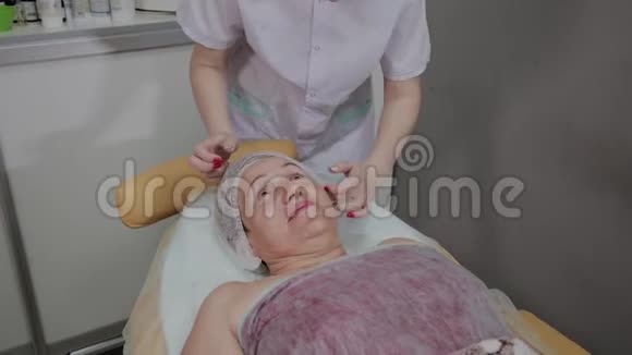 一位老年妇女躺在美容诊所的沙发上一位美容师正了正她的帽子视频的预览图