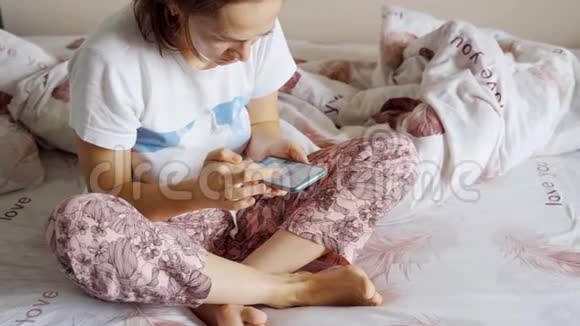 一个穿睡衣的女人坐在一个挺直的沙发上手里拿着一部智能手机视频的预览图