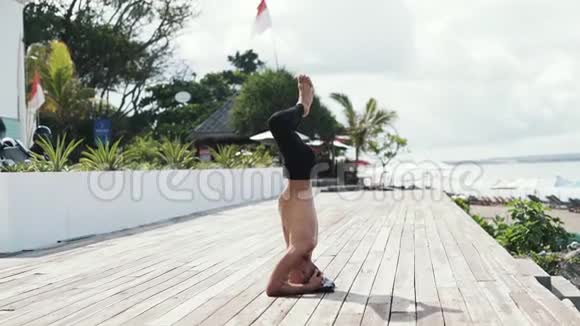 动作缓慢的运动型男子站在头部海洋和手掌上做瑜伽运动视频的预览图
