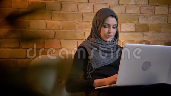 戴头巾的穆斯林成年女性的特写肖像在坐在沙发上用笔记本写一篇文章视频的预览图