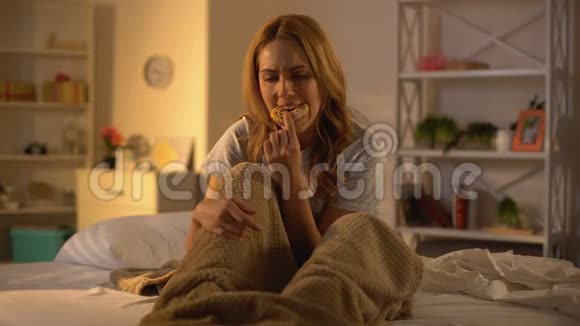 沮丧的女人坐在床上咀嚼甜甜圈压力过大不健康的食物视频的预览图