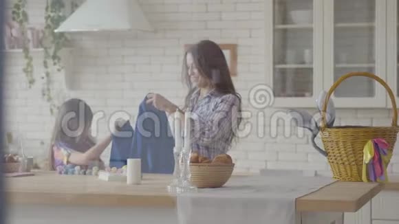 漂亮的女人和小女孩在厨房里穿蓝色围裙准备复活节假期丙烯酸涂料瓶视频的预览图