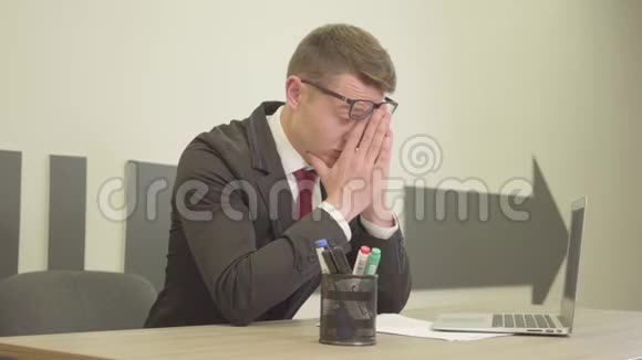 年轻的紧张压力很大穿着正式服装戴着眼镜坐在办公室前的笔记本电脑前擦着脸视频的预览图