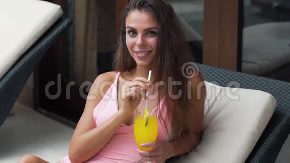 穿着泳衣的漂亮女孩看着镜头微笑着喝橙汁慢动作视频的预览图