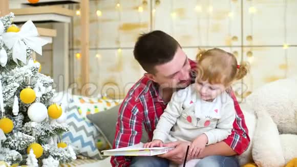 小女孩坐在她父亲的腿上在圣诞树旁用铅笔玩得很开心视频的预览图