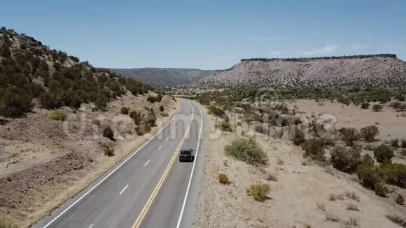 在美国亚利桑那州夏天Drone沿着银色的小型货车行驶在雄伟的阳光明媚的沙漠山路上公路旅行假期视频的预览图