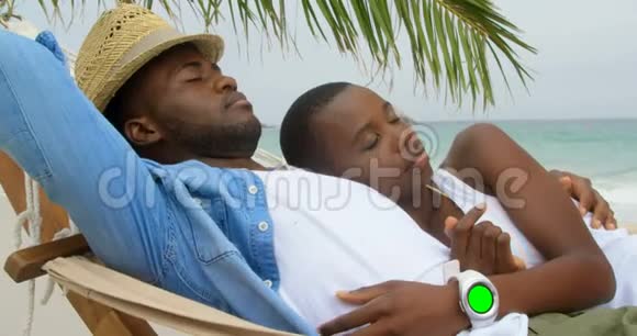 在海滩上睡在吊床上的非裔美国夫妇的侧面景色视频的预览图