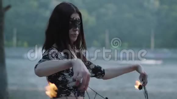 戴着面具的可爱优雅女人的肖像表演了一场表演火焰站在树前的河岸上技能视频的预览图
