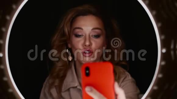 化妆师女人拿着智能手机在环形灯前自拍视频的预览图