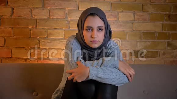 戴着头巾的年轻穆斯林女性在坐在室内沙发上看电视时感到惊讶的特写镜头视频的预览图