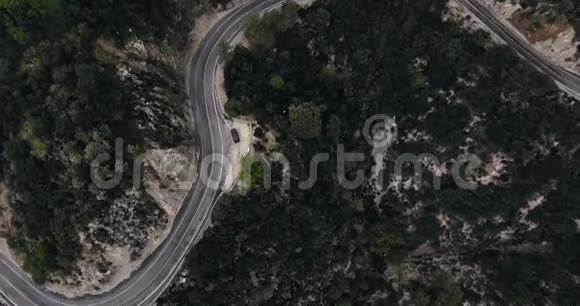 无人机拍摄了一辆停在山上一条蜿蜒的道路附近的黑色汽车那里有一片漆黑的森林视频的预览图