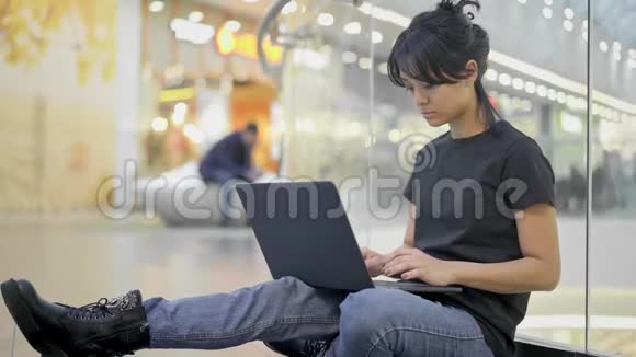 在购物中心购物中心一个年轻的亚洲女人拿着笔记本电脑坐在地上视频的预览图
