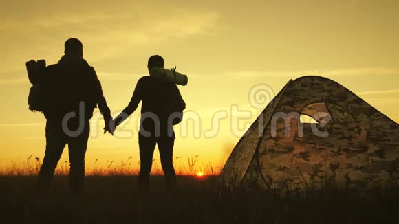 剪影旅游夫妇站在度假帐篷附近手牵手看日落营地休息生活方式视频的预览图