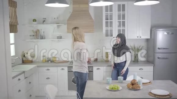 穆斯林妇女戴着头巾在家里和金发白种人朋友争吵两个女人在室内争吵误解视频的预览图