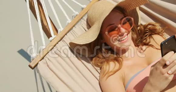高角度视角的高加索女人使用手机在海滩吊床4k视频的预览图