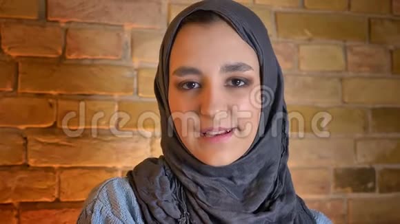 年轻迷人的穆斯林女性戴着头巾直视镜头在舒适的室内欢快地微笑视频的预览图