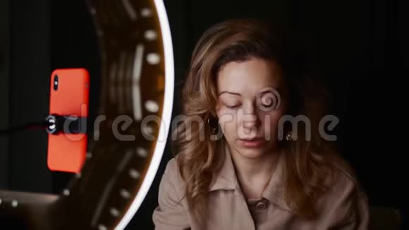 成熟的女人在黑暗的房间里在环灯前拍摄美容教程视频的预览图