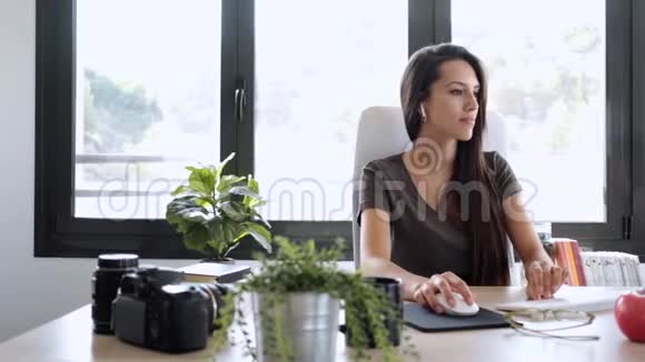 在办公室听音乐时微笑着用电脑工作的年轻商务女性视频的预览图