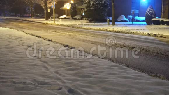 白雪皑皑的夜晚覆盖了住宅区的乡村道路汽车灯光小径视频的预览图
