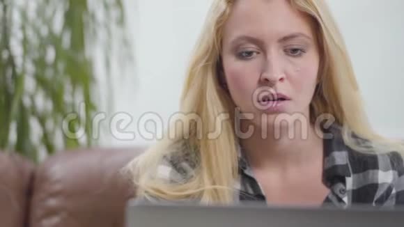 那个金发女孩坐在笔记本电脑前的皮革沙发上看着笔记本电脑屏幕震惊那个女人视频的预览图