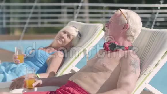 成熟的夫妇躺在游泳池附近的日光浴床上喝着果汁交谈着微笑着充满爱意的家庭康乐及文化事务署视频的预览图