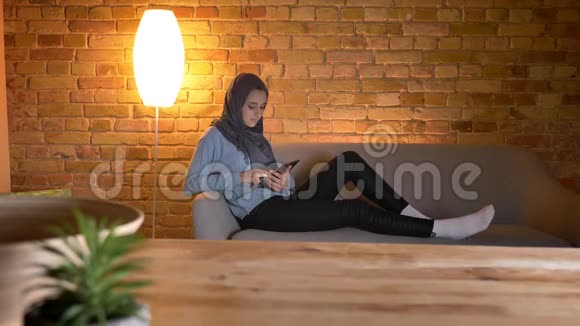 年轻迷人的穆斯林女性在舒适的家中悠闲地休息时在手机上上网特写镜头视频的预览图