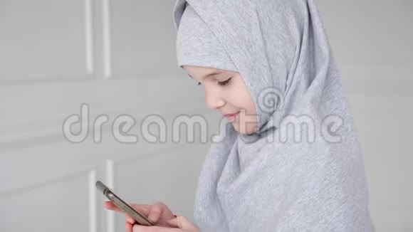 戴着头巾的年轻穆斯林少女正在玩智能手机害羞地看着相机微笑着视频的预览图