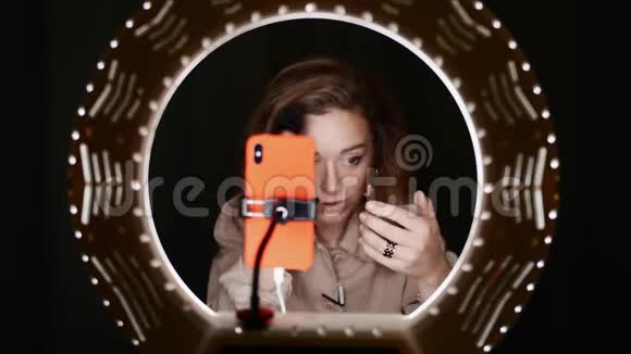 可爱的女性博客写手用手机在灯光前的面部轮廓视频的预览图