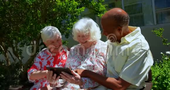 一组活跃的混合种族高级朋友在养老院花园使用数字平板电脑4k视频的预览图